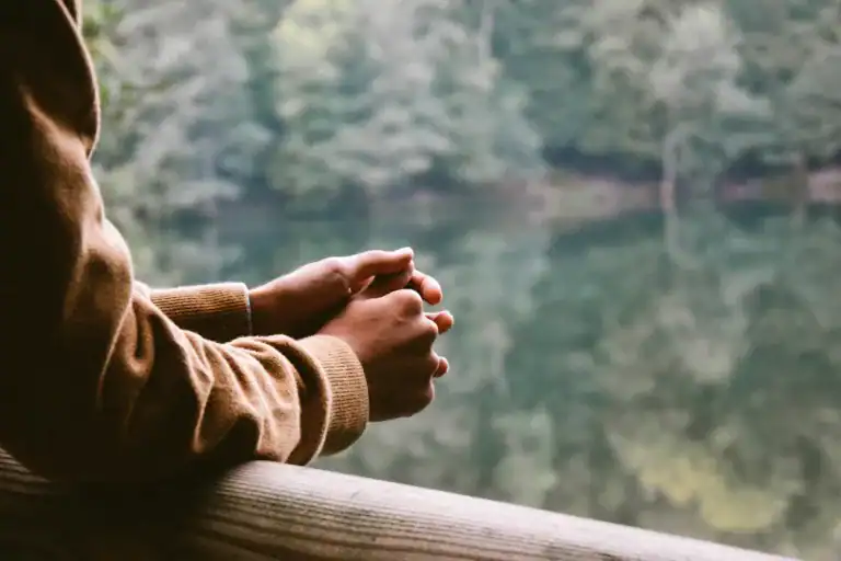 How To Take Care Of Your Mental Health As A New Mom: The Ultimate Guide 1 woman sitting with hands folded by a lake